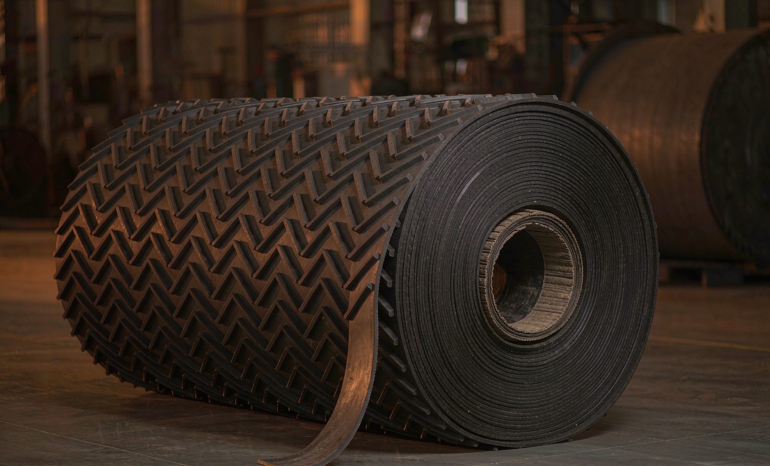 Rolled black rubber conveyor belt with chevron cleats showing fabric plies